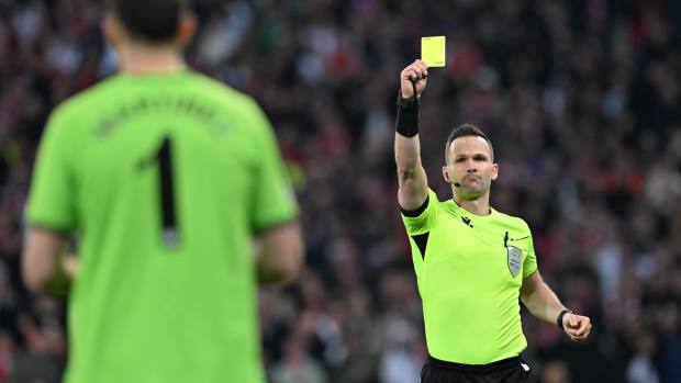 Referee Ivan Kruzliak pictured showing a yellow card to Emiliano Martinez during a UEFA Europa Conference League quarter-final between Lille and Aston Villa in April 2024