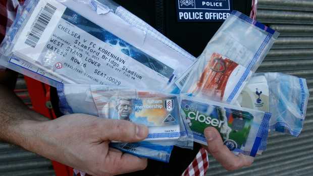 A police officer poses for photographs with English Premier League soccer club membership cards and UEFA Champions League match tickets recovered from a suspected ticket tout, during a search at the address of a furniture shop