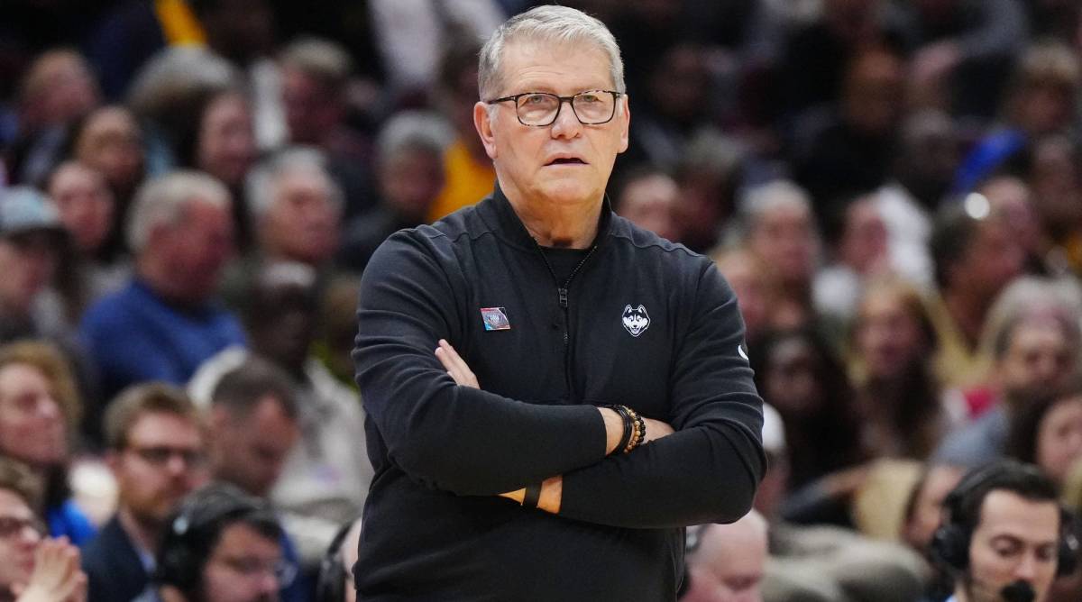 UConn head coach Geno Auriemma looks on with his arms crossed while coaching in a game.