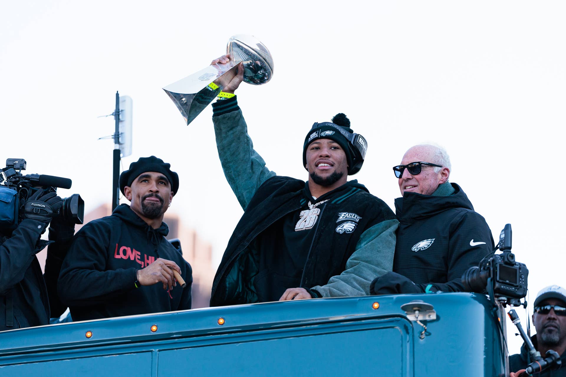 Eagles running back Saquon Barkley lifts the Lombardi Trophy with Jalen Hurts (L) and Jeffrey Lurie (R)